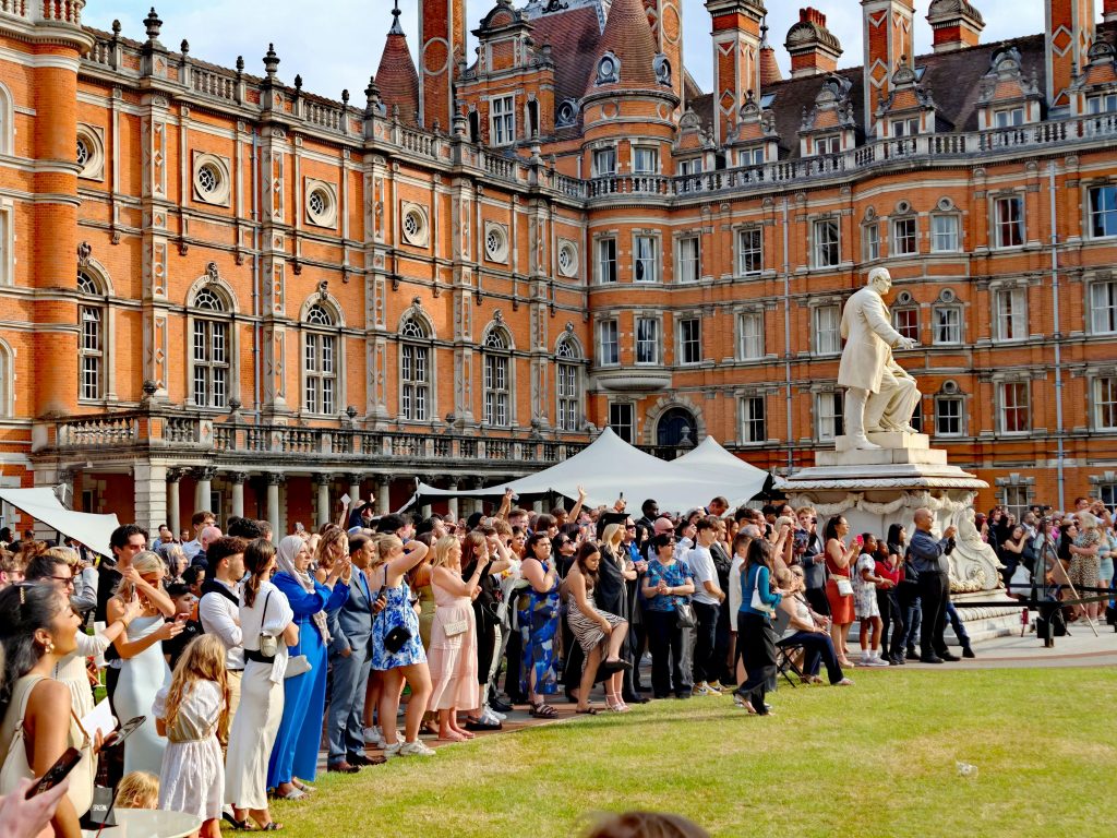 A large crowd gathers for a graduation ceremony at a historic university in England, featuring ornate architecture. GREAT Scholarships