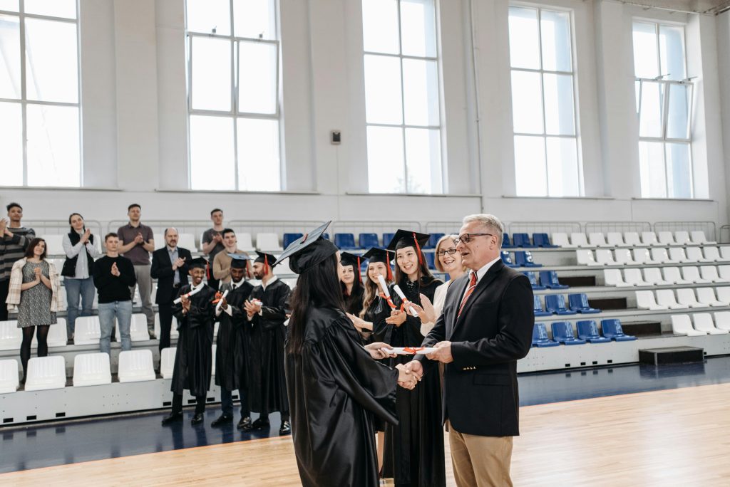 Students receive diplomas at a joyful graduation ceremony inside a gymnasium.