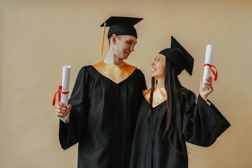 Two happy graduates in caps and gowns celebrating their achievement indoors. Allan and Nesta Ferguson Scholarships at the University of Leeds for 2025