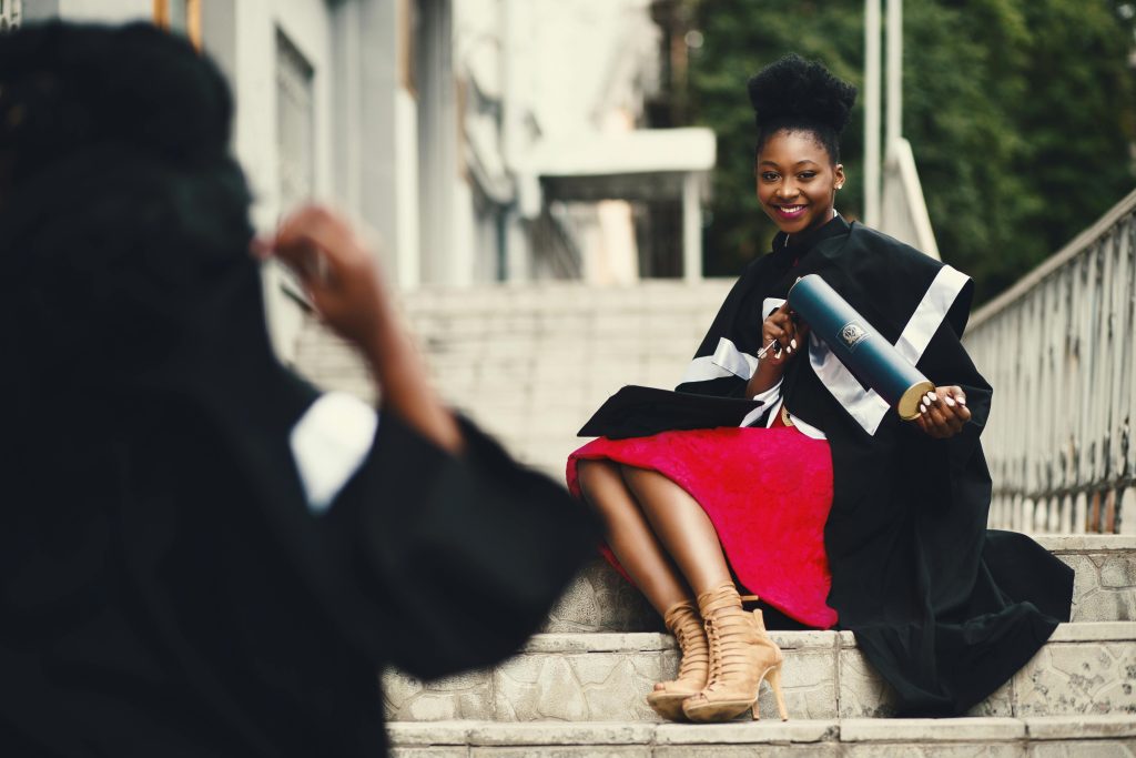 Project management at Arden University features a black female graduate in a gown smiling.